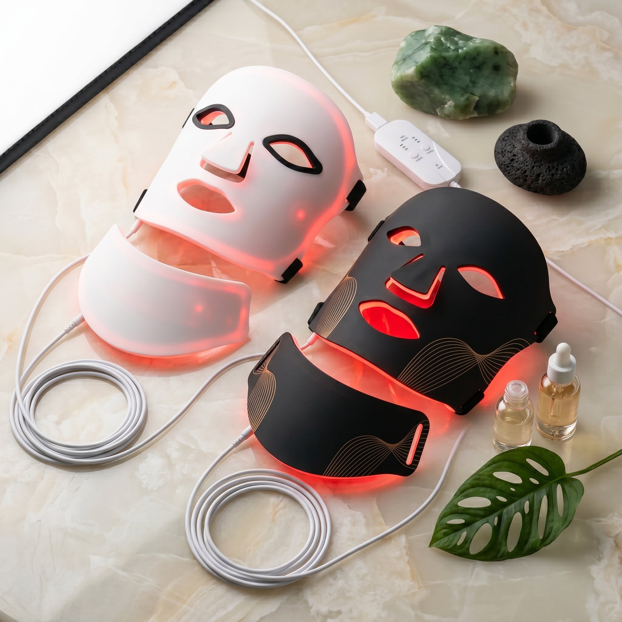 Two LED face masks on a marble surface with a plant and bottles in the background.
