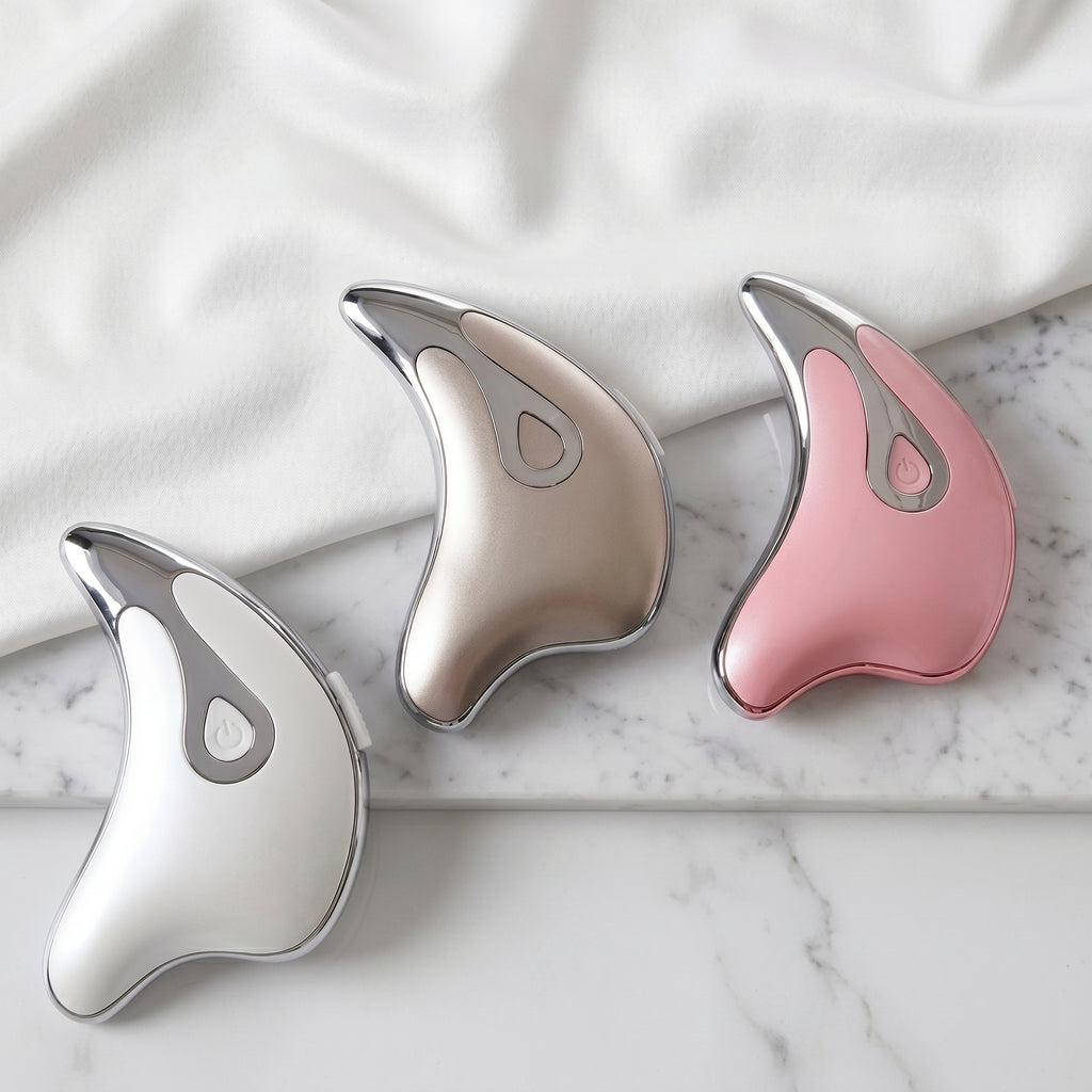 Three gua sha tools in silver, pink, and white.