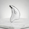 Silver Gua Sha tool on a marble surface with a light gray background